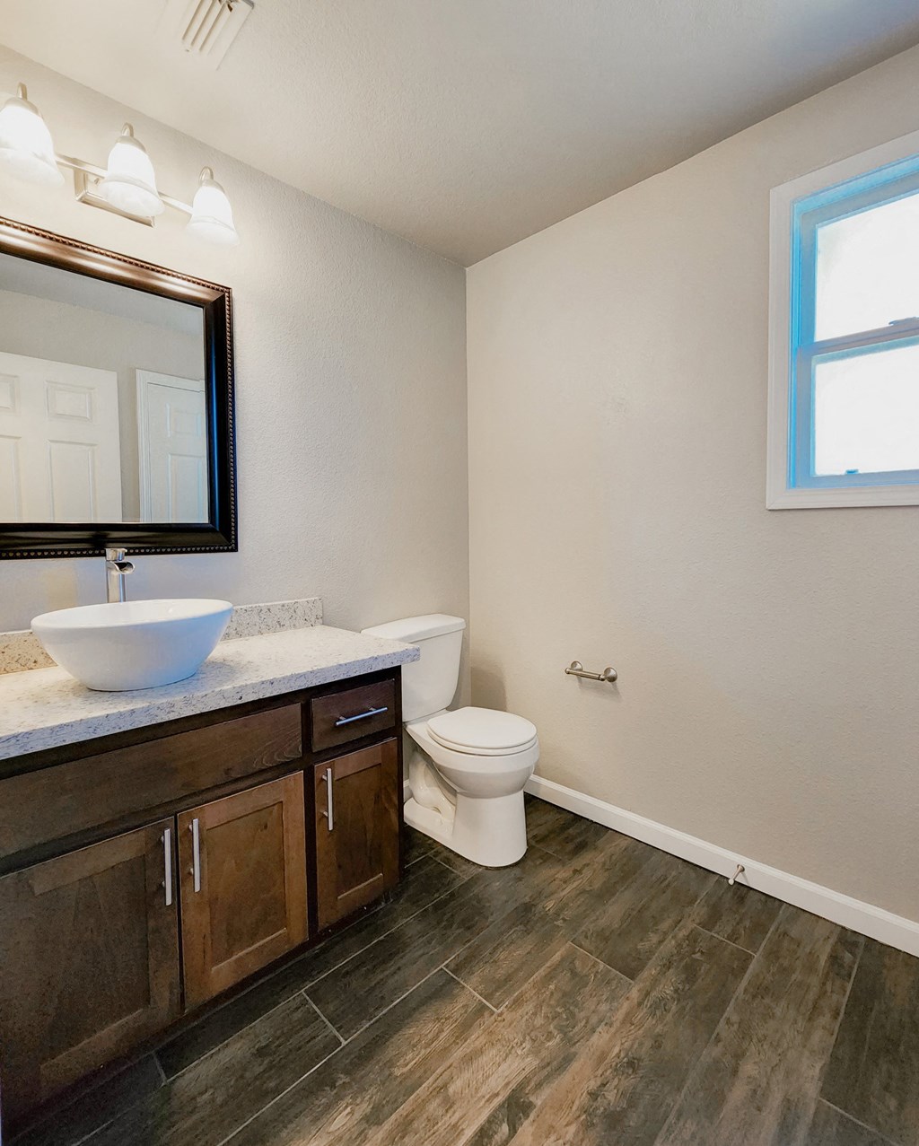 View of bathroom vanity with vessel sink, large mirror, toilet, and well lit window.
