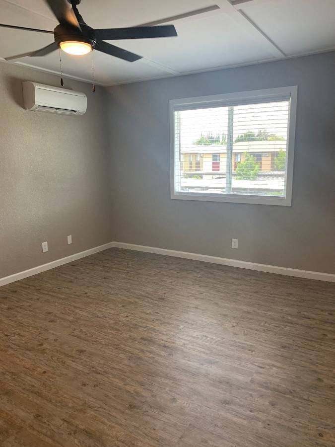 View of living area with wood like flooring, well lit window, veiling fan, and AC