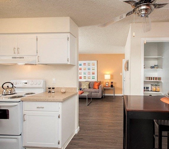 View of kitchen and into living area featuring white cabinets, white appliances, wood look flooring, full size pantry, and couch in living area