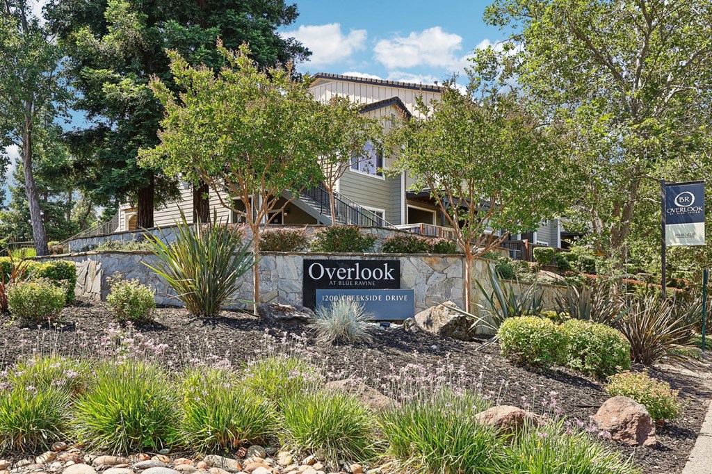 a sign in front of an apartment with trees and plants