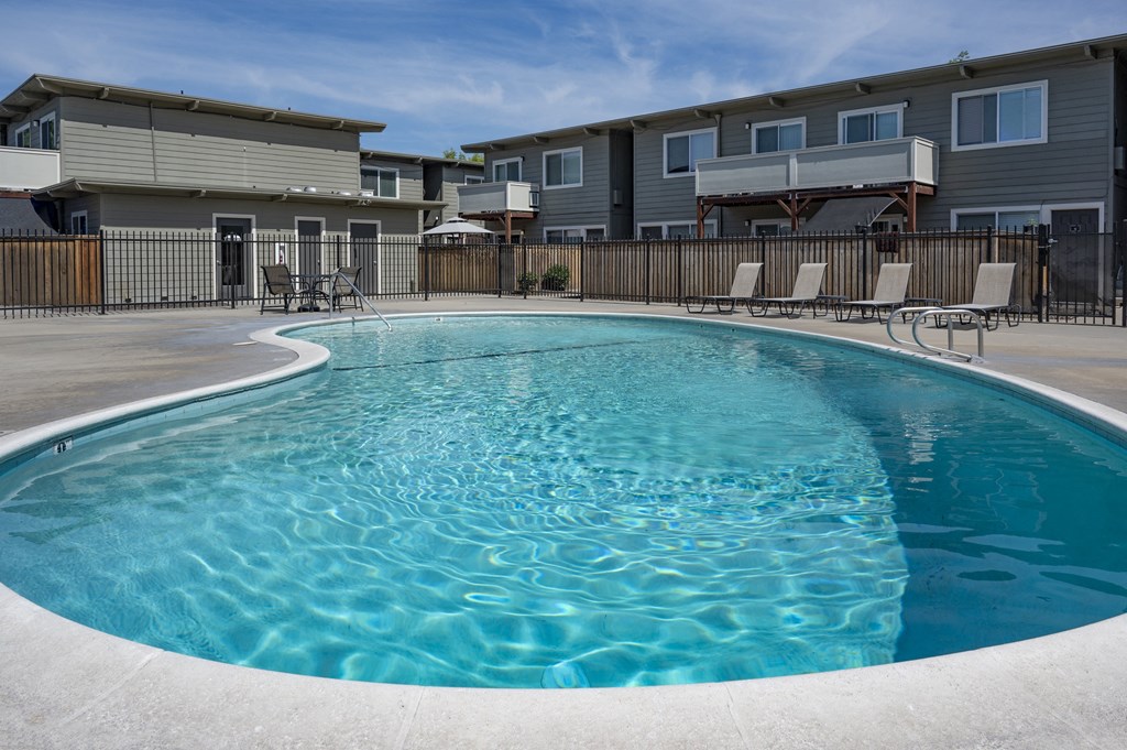 a swimming pool with chairs around it in front of an apartment building