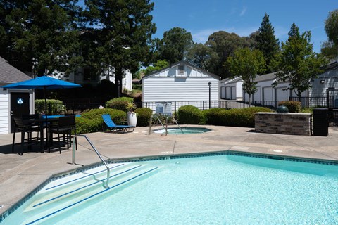 A swimming pool with a blue umbrella and a white house in the background.