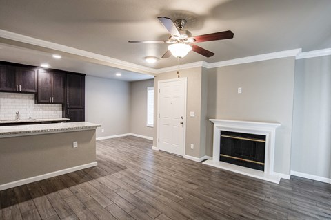 View from living room into kitchen and dining, with wood like flooring, ceiling fan, fireplace, view of bar countertop, tile backsplash, and brown cabinets