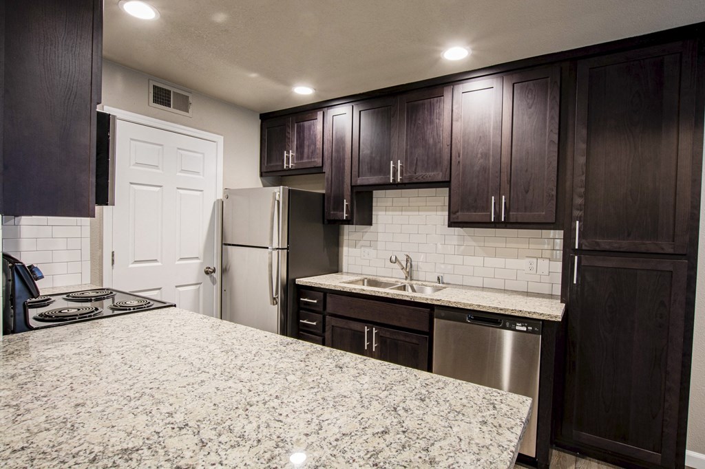 Alternate view of kitchen with stone counters, tile backsplash, stainless appliances, brown cabinets