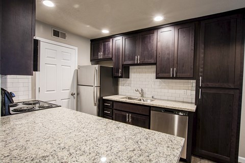 Alternate view of kitchen with stone counters, tile backsplash, stainless appliances, brown cabinets
