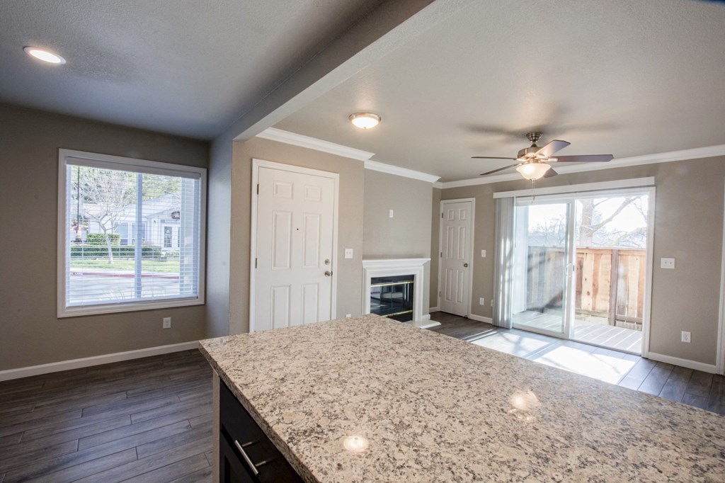 View from kitchen bar top into living room with fireplace and access to private balcony/patio through sliding glass door, with well lit window