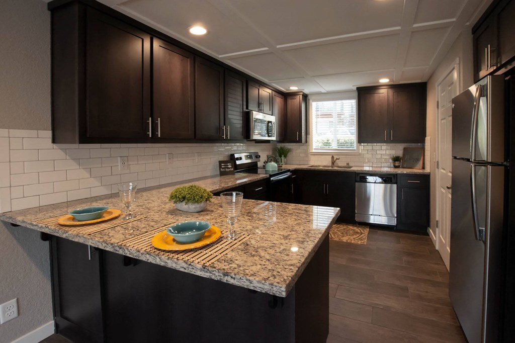 view of kitchen with stone counters, inlaid sink, well lit window above sink, brown cabinets, and stainless appliances