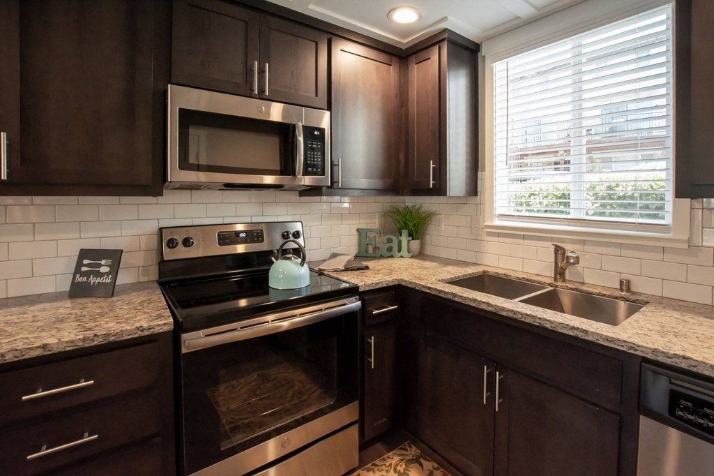 view of kitchen with stone counters, inlaid sink, well lit window above sink, brown cabinets, and stainless appliances