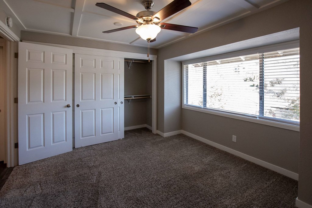 View of bedroom with carpet flooring, sliding door access to closet, ceiling fan, and well lit window