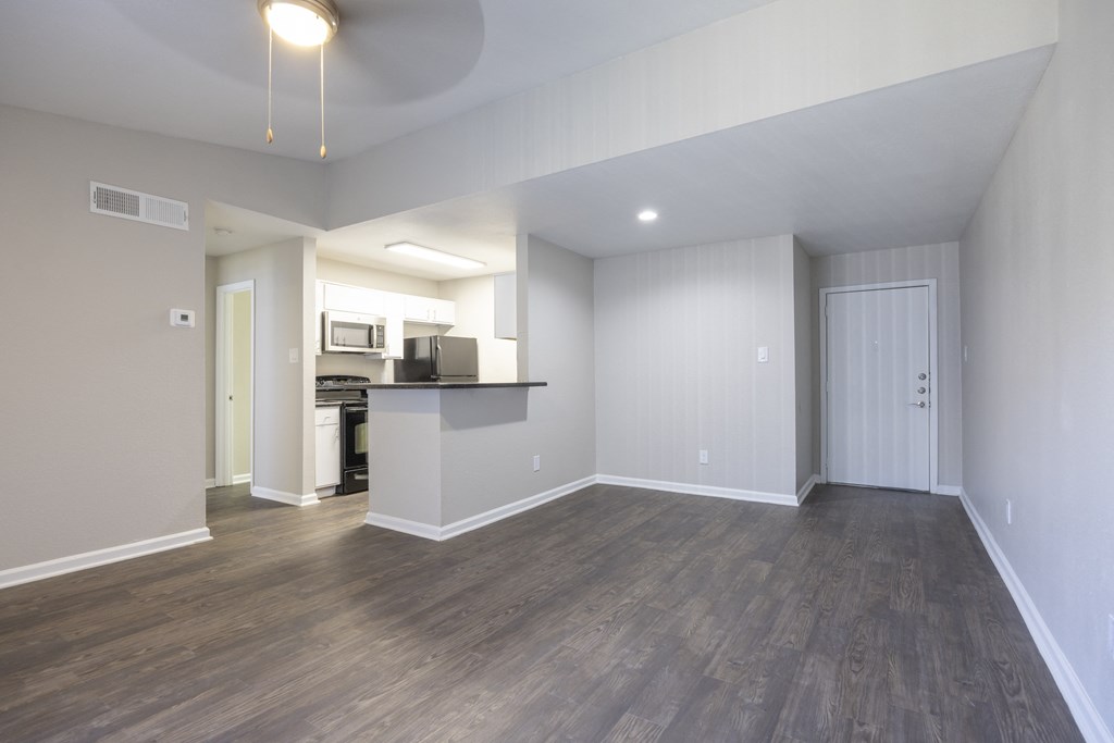 an empty living room with a kitchen in the background
