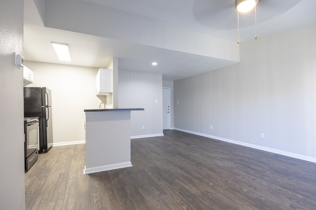 an empty living room with a kitchen and a counter top in the corner