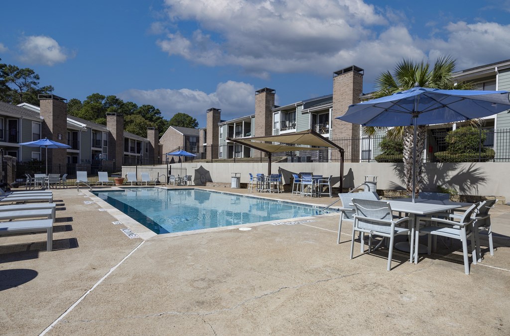 A pool area with chairs and umbrellas in front of a building.