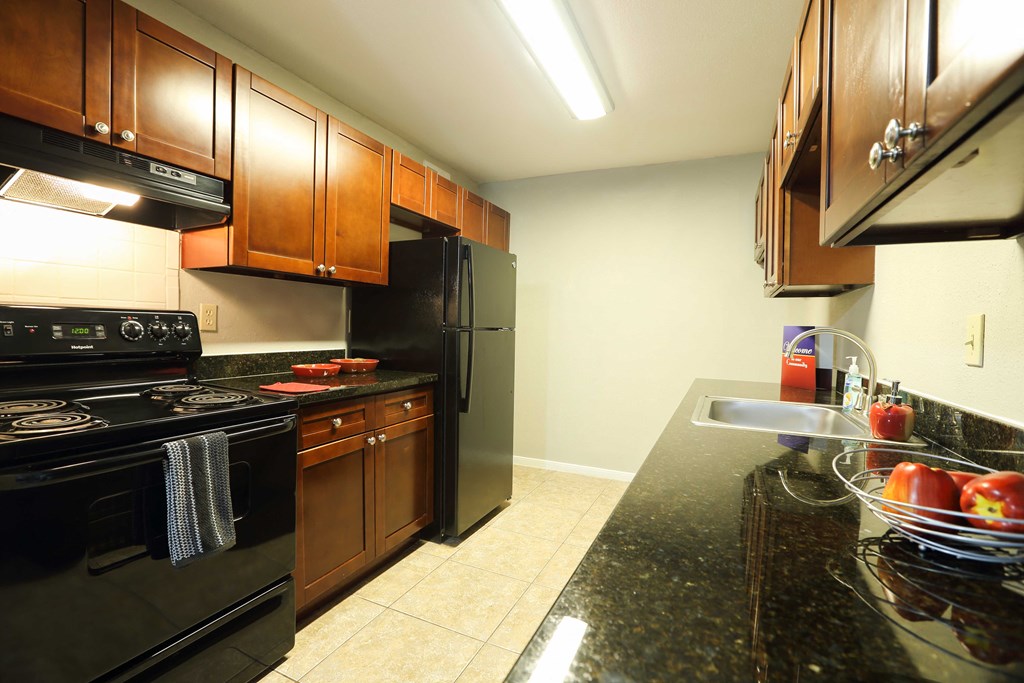 kitchen area with tile flooring, dark counters, black appliances, and brown cabinets