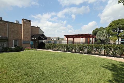 a grassy area with a pergola in front of a brick building