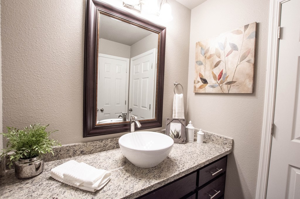 granite vanity with vessel sink, mirror, and lighting