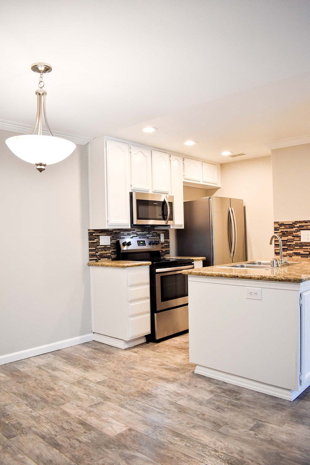 View of kitchen with stainless appliances, stone counters, tile backsplash, white cabinets and wood look flooring