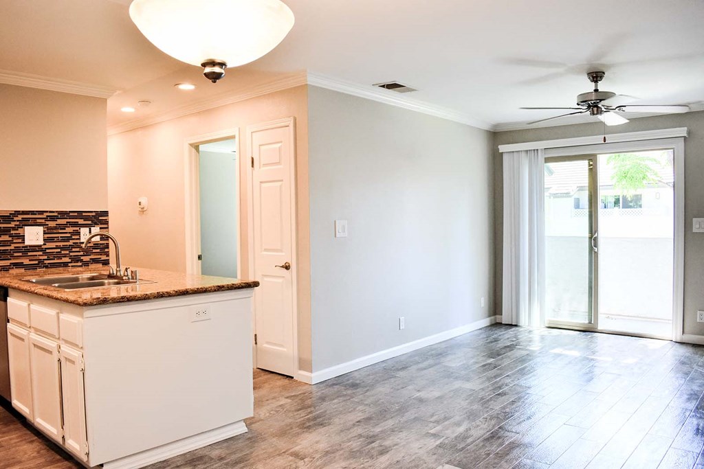 Living room view with wood look flooring, sliding glass door leading to private patio, partial view of kitchen counter