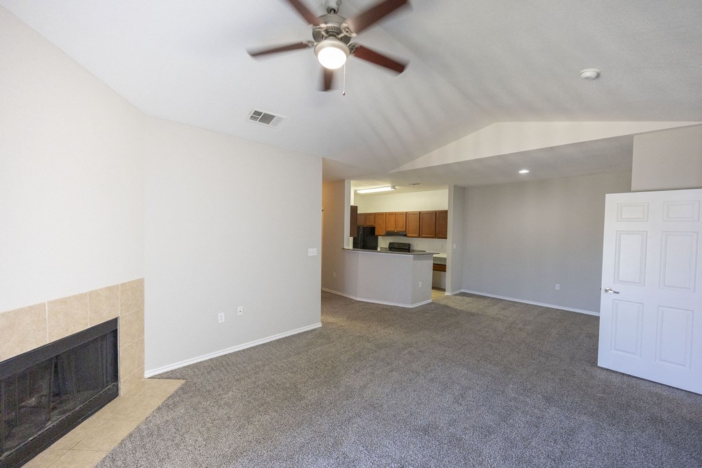 View from living area into dining and kitchen with vaulted ceiling and ceiling fan and light fixture, carpet flooring, and fireplace