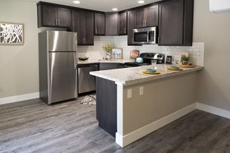 Kitchen with stainless appliances, stone counters, tile backsplash, wood look flooring, brown cabinets, and recessed lighting
