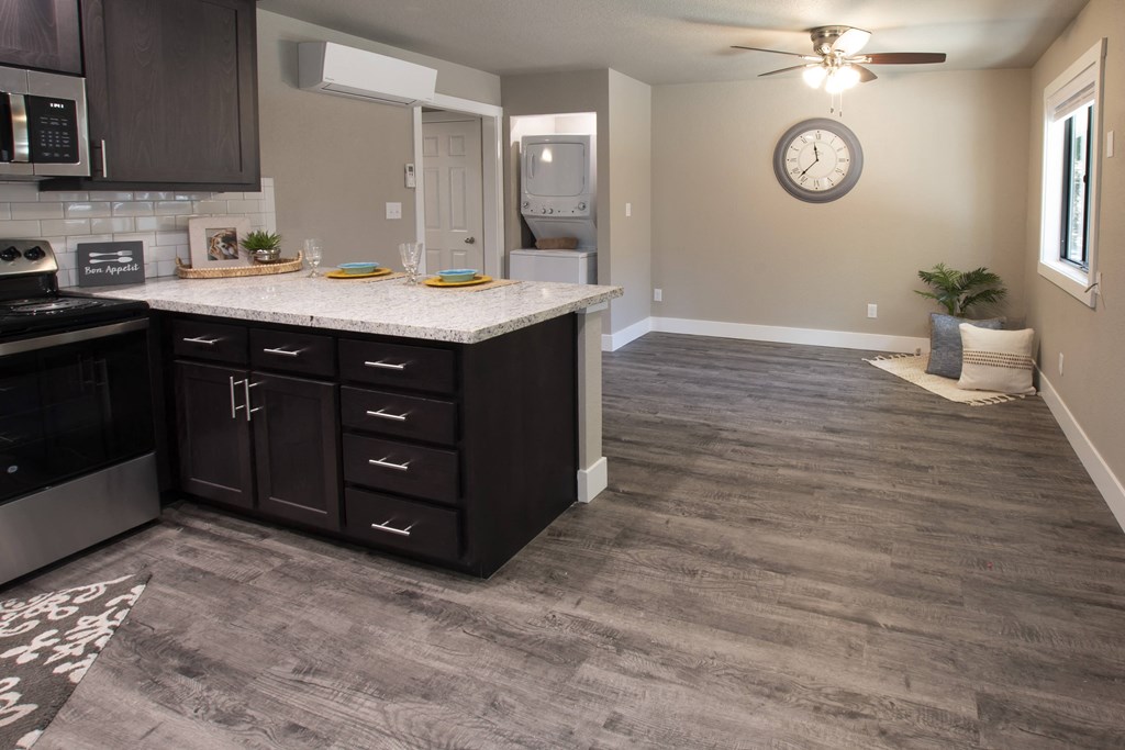 View from dining area into living area, stone counters with brown cabinets, wood look flooring, ceiling fan and well lit window