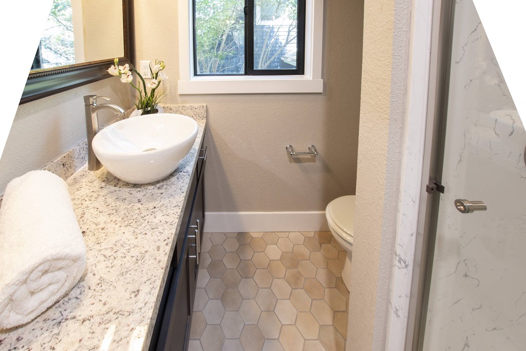 View of bathroom with stone vanity, vessel sink, large mirror, and well lit window
