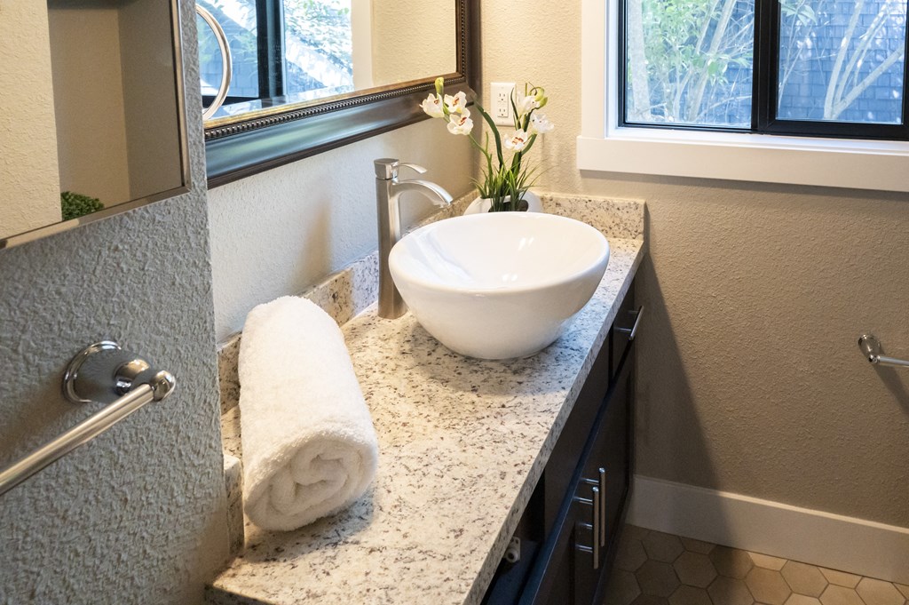 stone bathroom vanity with vessel sink, large mirror, and well lit window