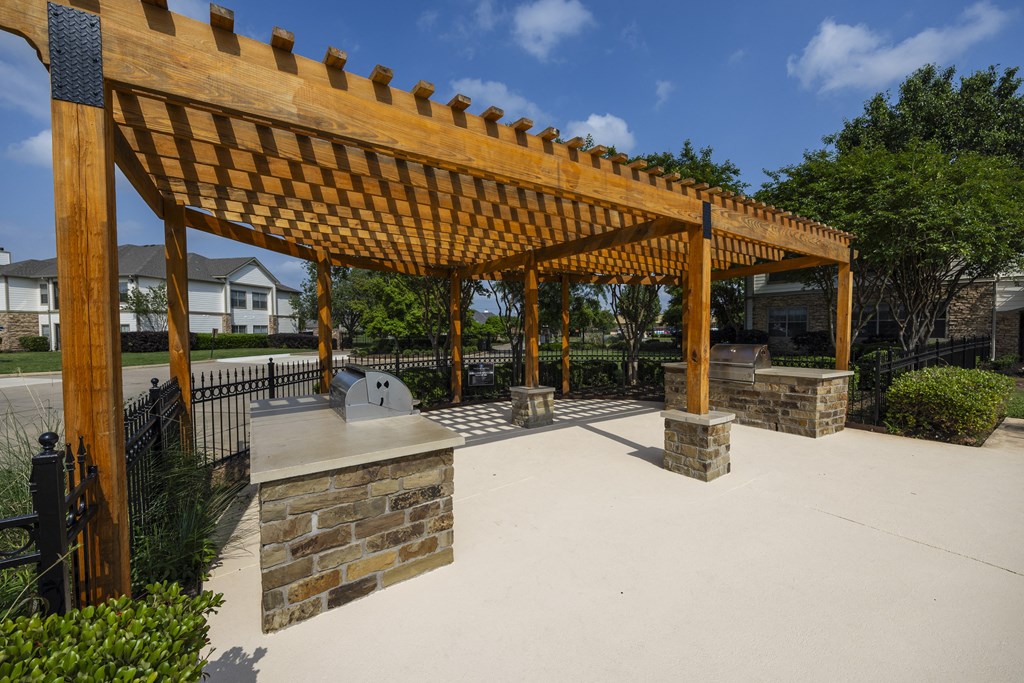 a covered patio with a stone fireplace and a wooden pergola