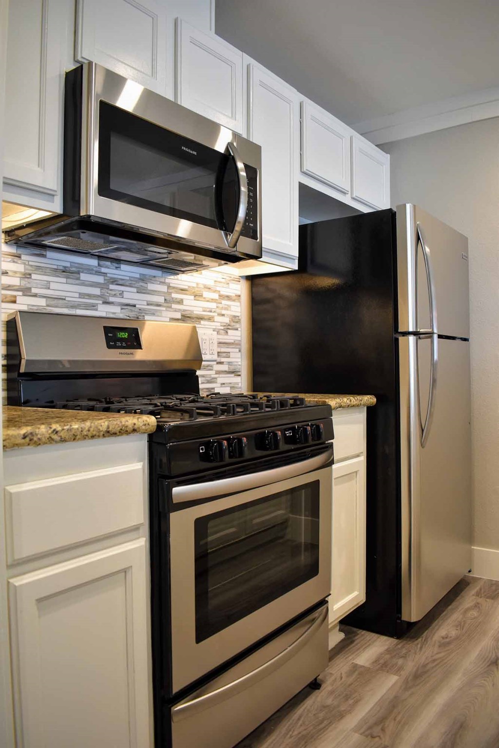 kitchen with stone counters, stainless appliances, tile backsplash, white cabinets