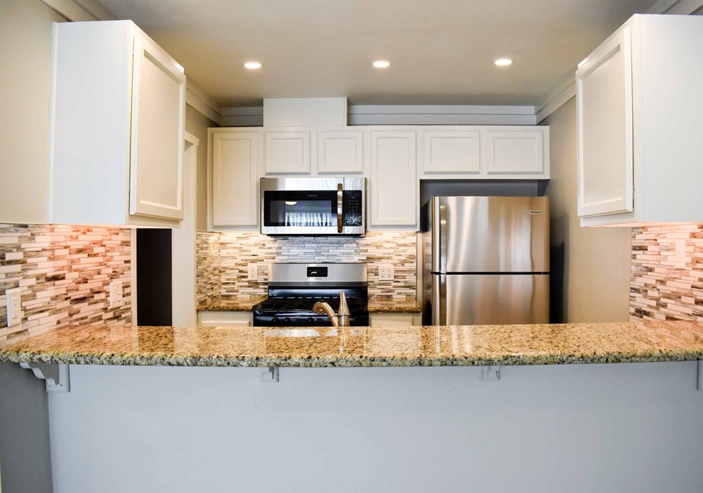 kitchen with stone counters, tile backsplash, stainless appliances, white cabinets, and recessed lighting