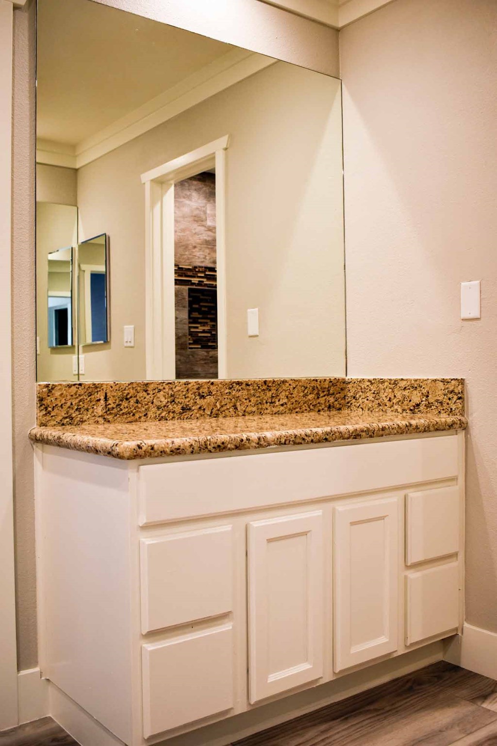 bathroom with stone vanity, large mirror, wood look flooring, and white cabinets