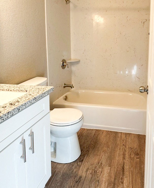 bathroom with wood look flooring, stone vanity, toilet, and tub shower combo