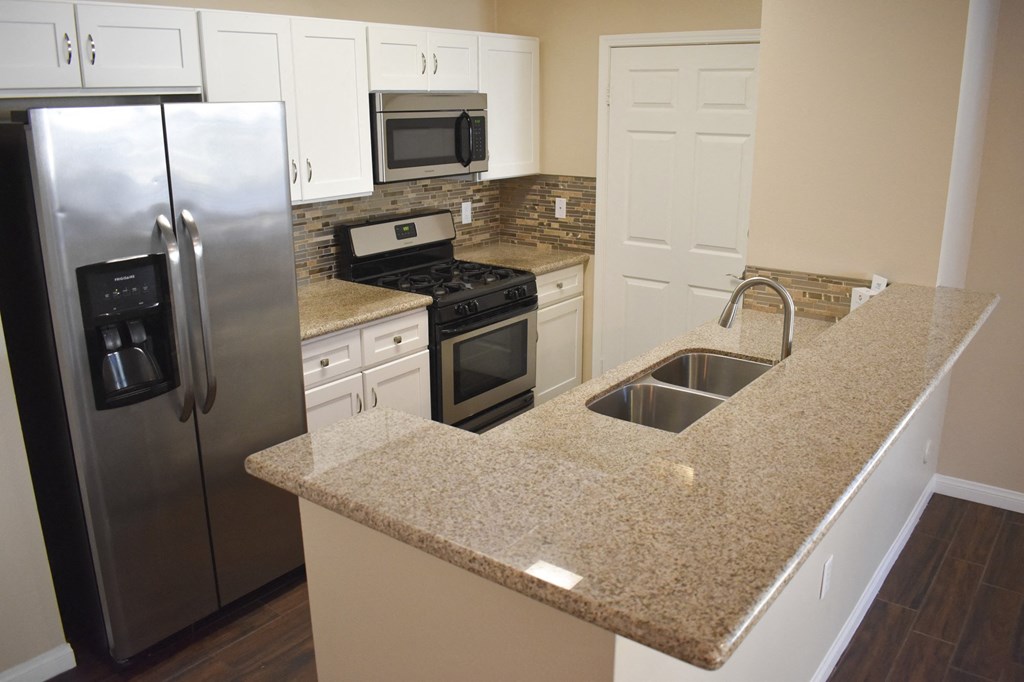 view of kitchen with stone counters, in laid sink, stainless appliances, and white cabinets
