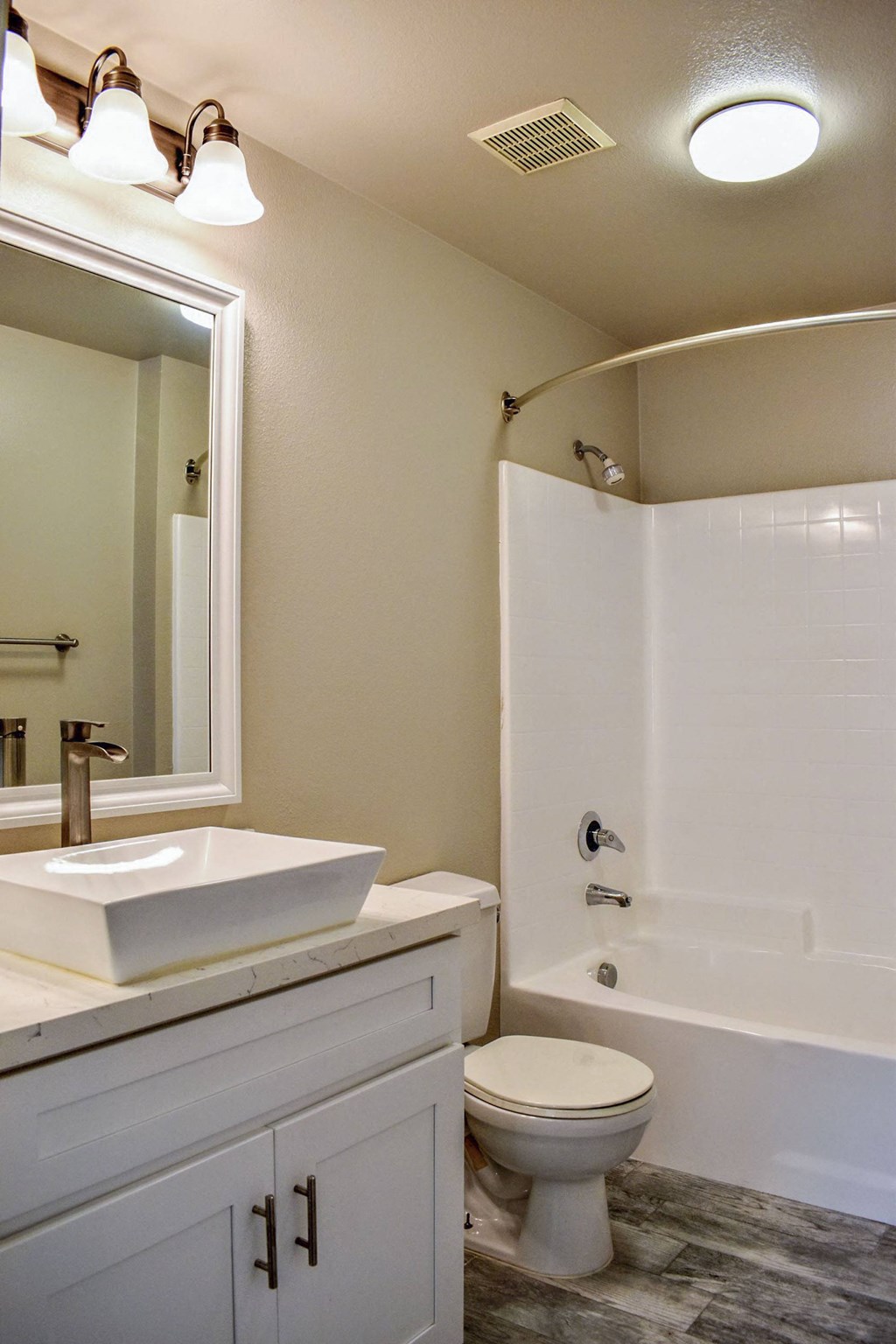 bathroom with vessel sink, large mirror with lighting, white cabinets, tub shower combo and toilet