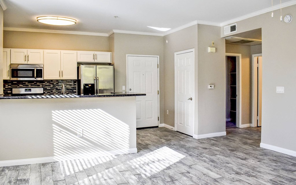 kitchen and dining area with wood look flooring, dark counters, white cabinets, tile backsplash, and stainless appliances.