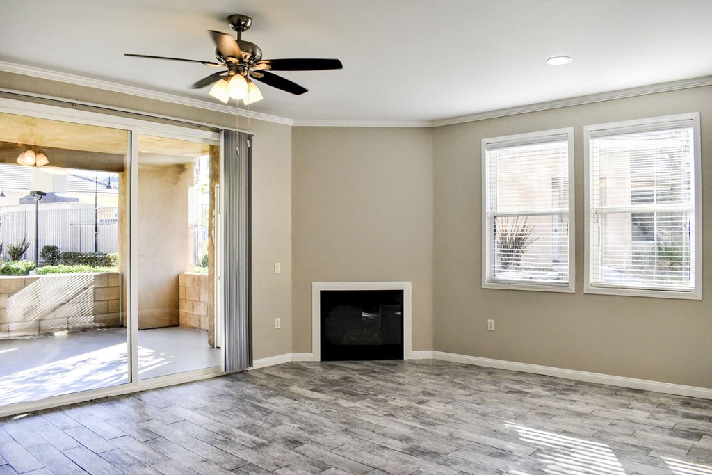 Living area with wood look flooring, two well lit windows, fireplace, ceiling fan, and access to private patio/balcony through sliding glass door