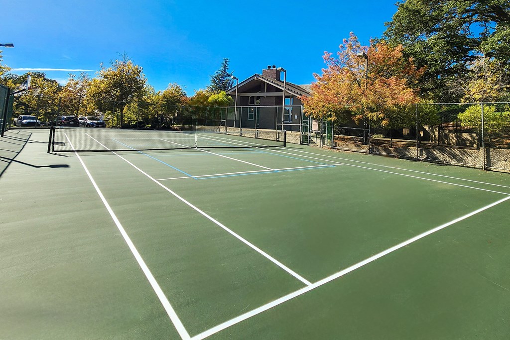 a tennis court with trees and a house in the background