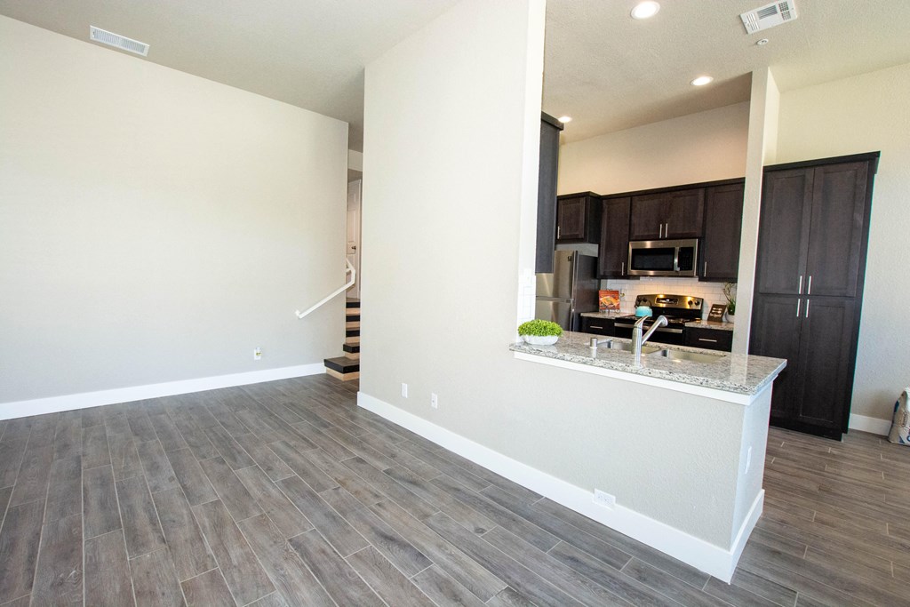 an empty living room with a kitchen and a hard wood floor