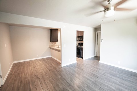 an empty living room with wood flooring and a kitchen