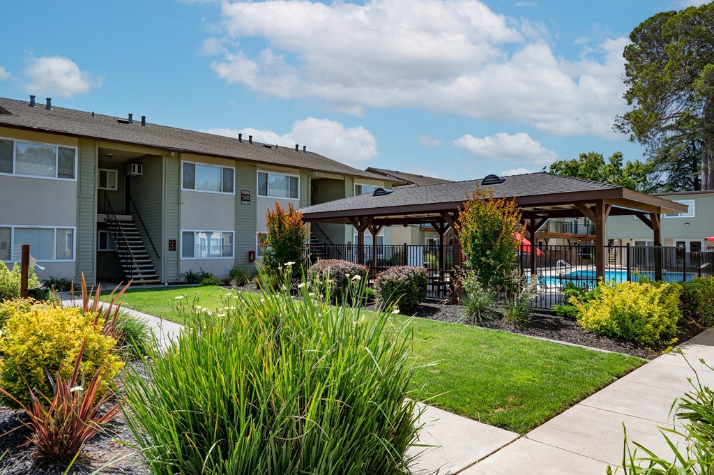 View of exterior building, well landscaped courtyard, gated pool area with covered area with picnic table and seating