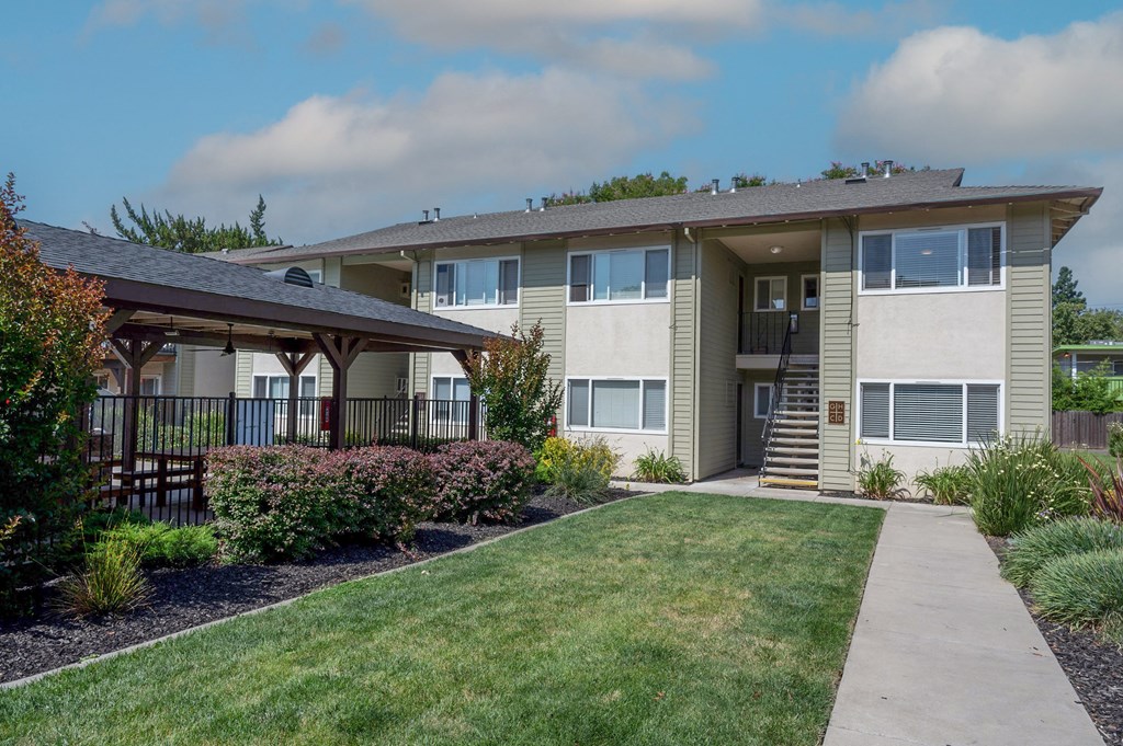 View of well landscaped courtyard with exterior building and gated community pool with covered area that has picnic table and seating