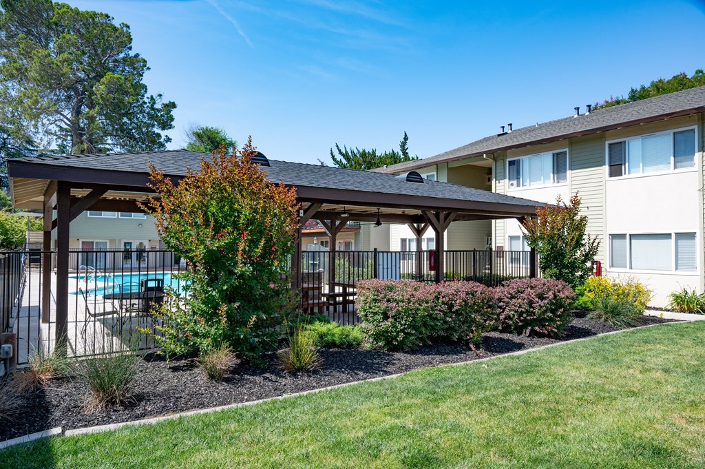 View of well landscaped courtyard with gated community pool in background. Has covered area with seating and picnic