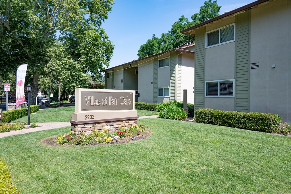 View of exterior of buildings with monument of Villas at Fair Oaks Logo