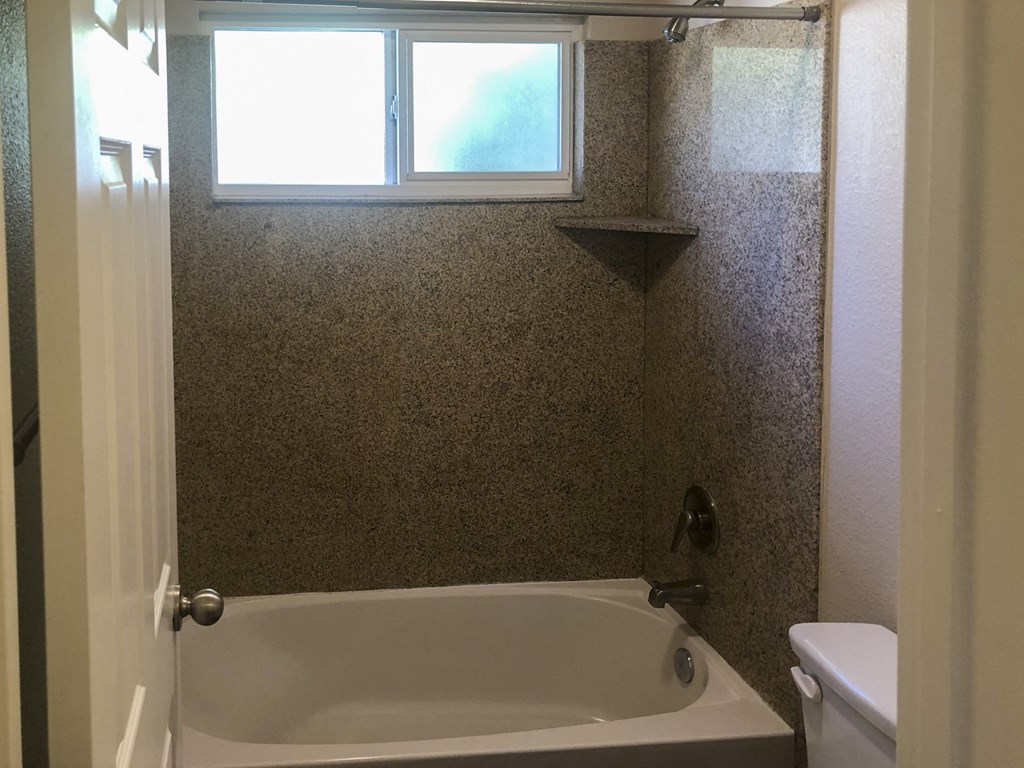 View of bathroom with toilet, tub shower combo and will lit window above tub