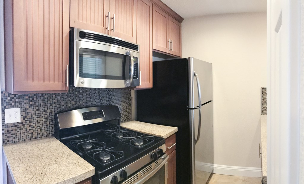 View of kitchen with stone counters, stainless appliances, tile backsplash, and brown cabinets