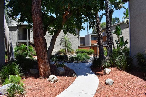 View of exterior buildings and side walk winding in between with lush landscaping and trees