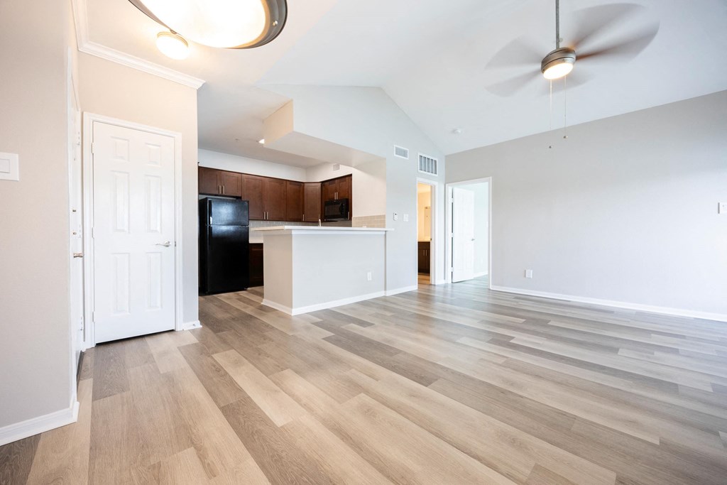 an empty living room with a kitchen and a ceiling fan