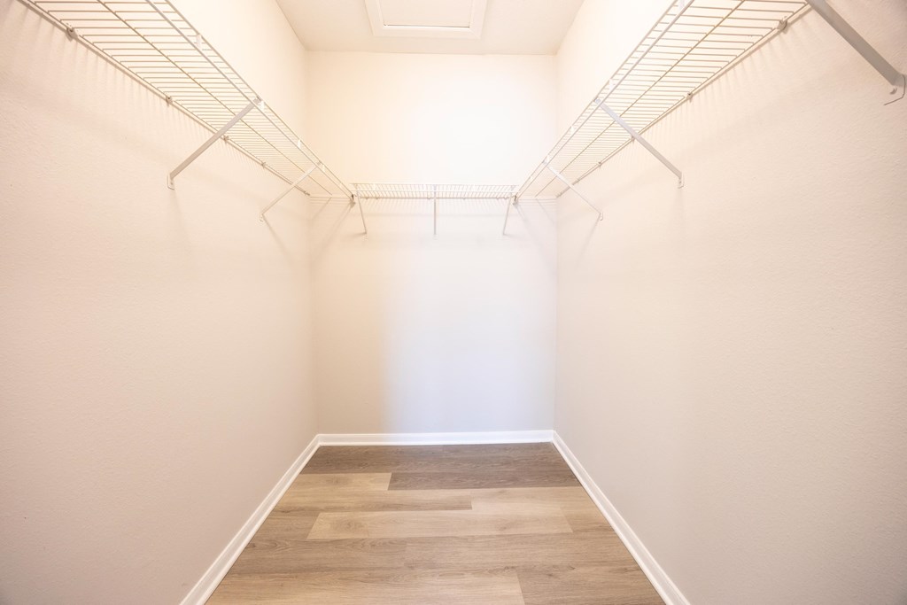 a walk in closet with white walls and wood flooring