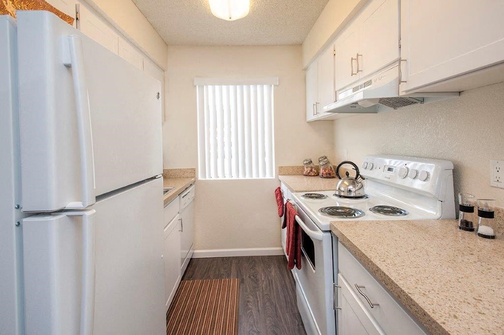 View of kitchen with wood like flooring, white cabinets, white appliances, and well lit window