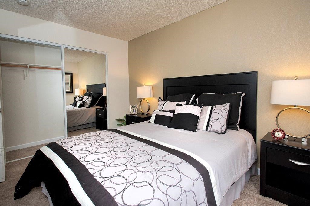 View of bedroom with sliding glass mirror closet with ample space to hang clothers, carpet flooring, and furnished as a model
