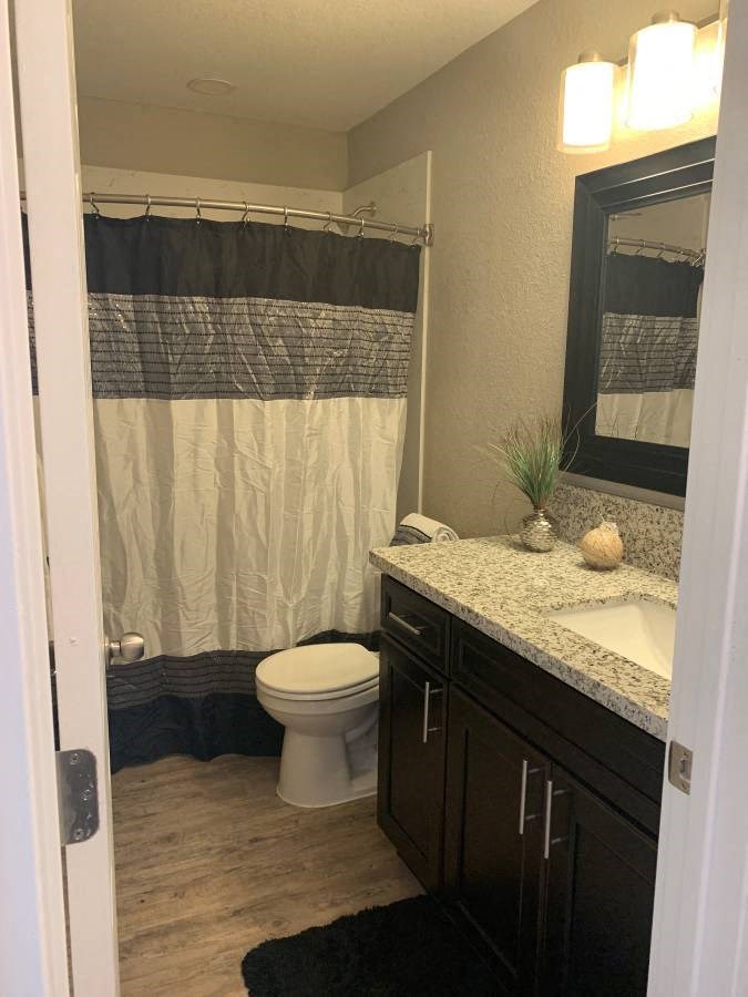 View of bathroom with large vanity, toilet, tub shower combo and wood look flooring